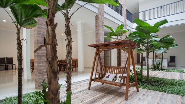 Un conjunto de columpios de madera en un espacio interior amplio, con pilares de ladrillo y plantas verdes.