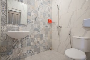 A bathroom with a tiled wall, a sink, a toilet, and a shower. - RedDoorz Syariah near Universitas Negeri Malang (Malang)