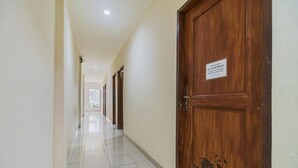 A hallway with a wooden door on the right, a sign above it, and a tiled floor. - RedDoorz @ Jalan Jenderal Sudirman Palembang 2 (Palembang)