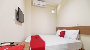 A hotel room with a bed, a TV mounted on the wall, an air conditioner, a small window, and a desk with a remote control and a red bag. - RedDoorz @ Jalan Jenderal Sudirman Palembang 2 (Palembang)