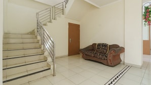 A staircase with metal railings leading to a door, a patterned sofa, and a patterned rug on a tiled floor. - RedDoorz @ Jalan Jenderal Sudirman Palembang 2 (Palembang)
