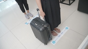 A person pulling a black suitcase with wheels, standing on a tiled floor with directional signs. - RedDoorz near Kranggan Tugu Jogja (Yogyakarta)