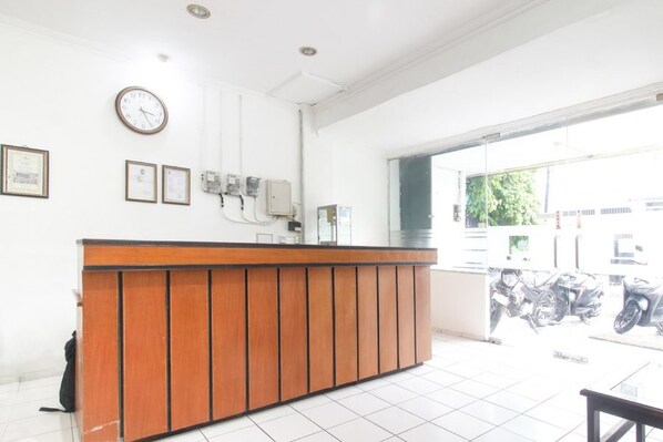 A reception desk with a clock, framed certificates, and a window with a view of parked motorcycles. - RedDoorz near Kranggan Tugu Jogja (Yogyakarta)