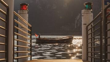 Un barco atracado en un muelle con barandillas a ambos lados, un faro al fondo y una superficie acuática tranquila que refleja la luz del sol.