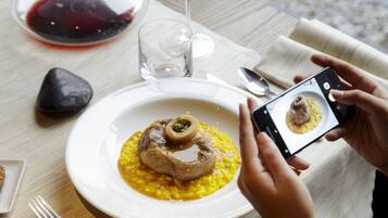 Une table à manger avec une assiette de nourriture, un verre de vin rouge et un téléphone intelligent utilisé pour prendre une photo.