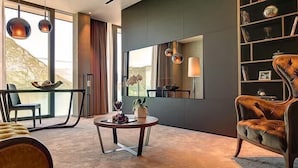 Una sala de estar moderna con un sofá, una mesa redonda de centro y una silla. Hay una estantería con diversos objetos y un espejo grande en la pared.
