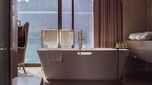 Un baño moderno con una bañera independiente, un tocador con espejo y vistas a una montaña y un cuerpo de agua.