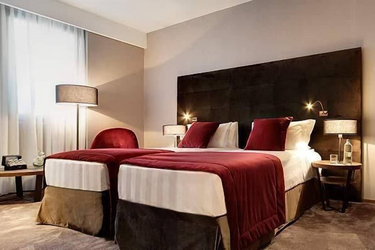 Una camera d'albergo con un letto grande, due comodini, una scrivania con una sedia e una lampada.