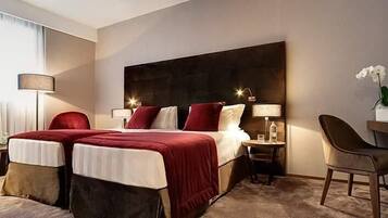 A hotel room with a large bed, two bedside tables, a desk with a chair, and a lamp.