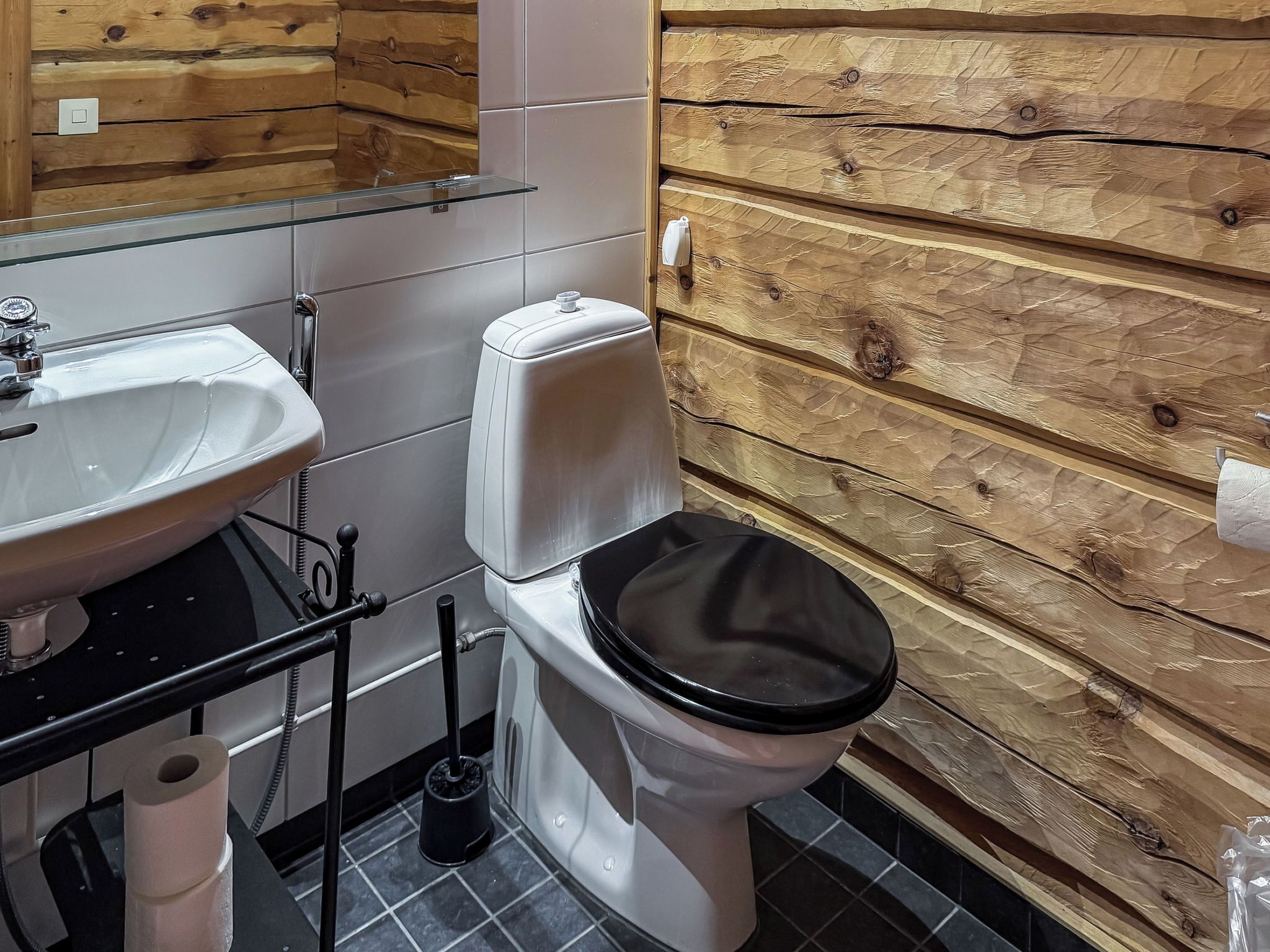 Un baño con pared de madera, un lavamanos blanco, un inodoro y un espejo.