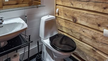 Un baño con pared de madera, un lavamanos blanco, un inodoro y un espejo.