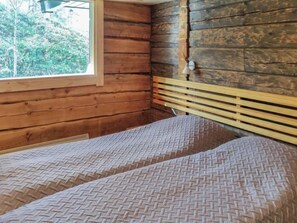 Relax in a cabin-style bedroom with a view of lush greenery outside, featuring a bed with a woven mattress and wooden headboard.