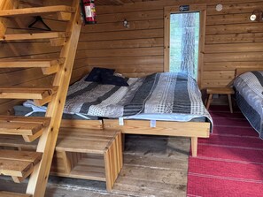 Une pièce de cabane en bois avec un lit en mezzanine, une petite table et un tapis rouge.
