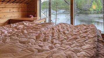 A bedroom with a large bed, wooden walls, a window overlooking a lake, and a small table with a bowl.