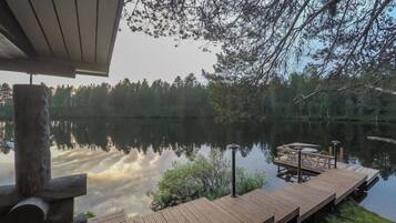 A wooden dock extending into a calm lake, surrounded by trees and a clear sky.