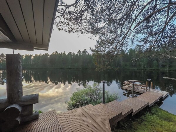 A wooden dock extending into a calm lake, surrounded by trees and a clear sky.
