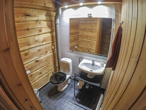 Bathroom features a toilet, sink, and mirror, with a tiled floor and wooden walls.