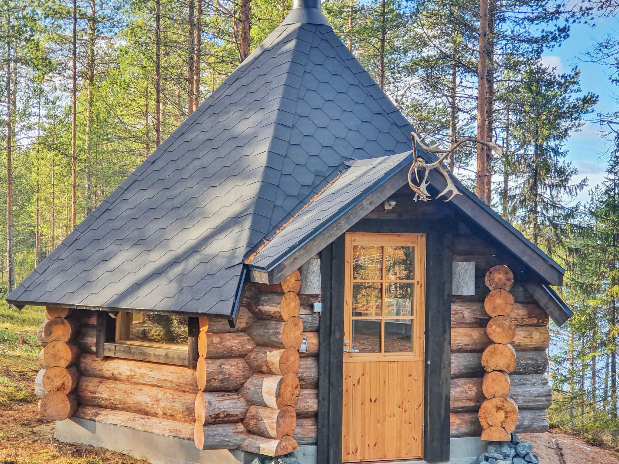 A log cabin with a conical roof, a wooden door, and a window.