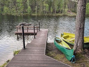 A wooden dock extending into a calm lake, with a green and yellow canoe tied to a tree.