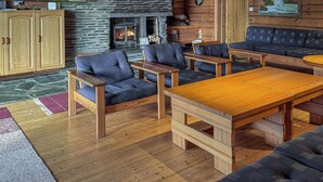 A cozy living room with a fireplace, wooden furniture, and a view of a mountainous landscape. - Sompsanniemi by Interhome (Kuusamo)