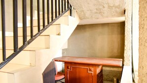 Un escalier avec des rampes noires, un bureau en bois et une chaise dans une pièce dont le mur est texturé.