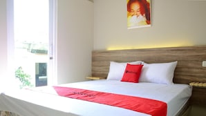 Un lit bien fait, avec une literie blanche et rouge, une tête de lit en bois et un tableau accroché au mur.