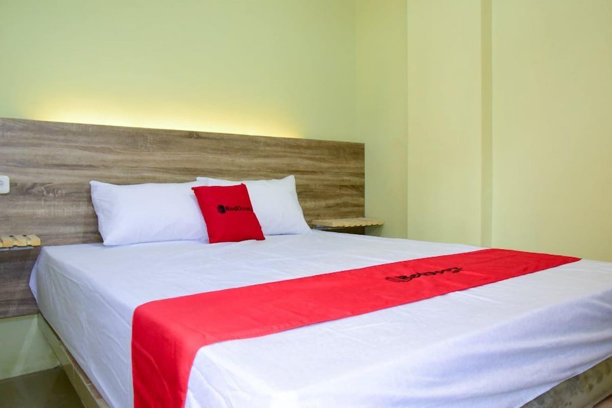 A bed with a white and red bedspread, a wooden headboard, and a pillow with a logo.