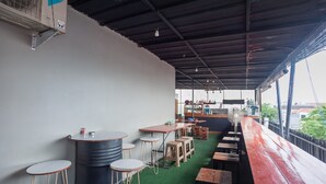 A restaurant with a long counter, stools, and a bar area. - RedDoorz Plus @ Kemayoran (Jakarta)