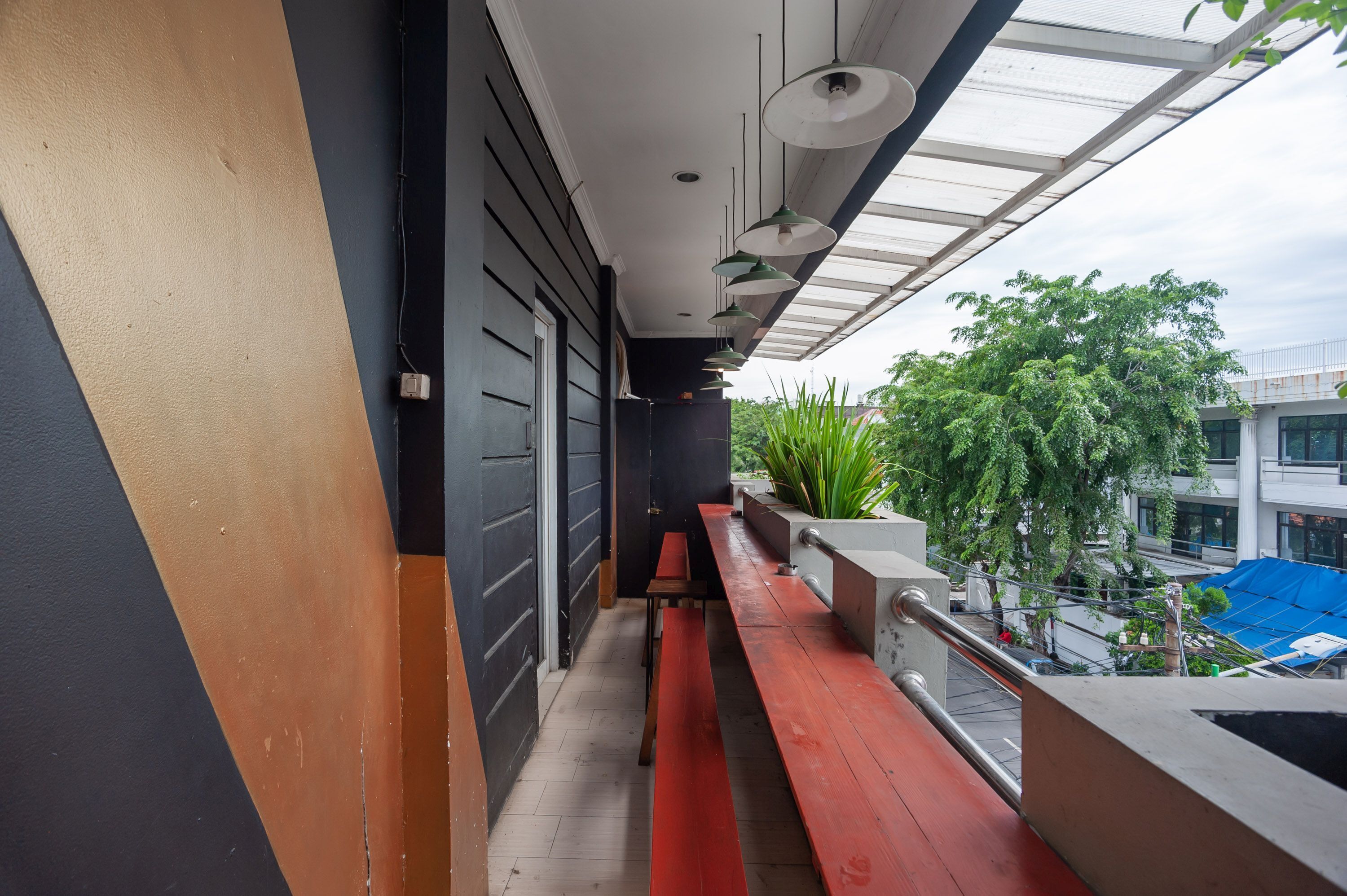 A narrow balcony with a red bench, a small table, and a potted plant.
