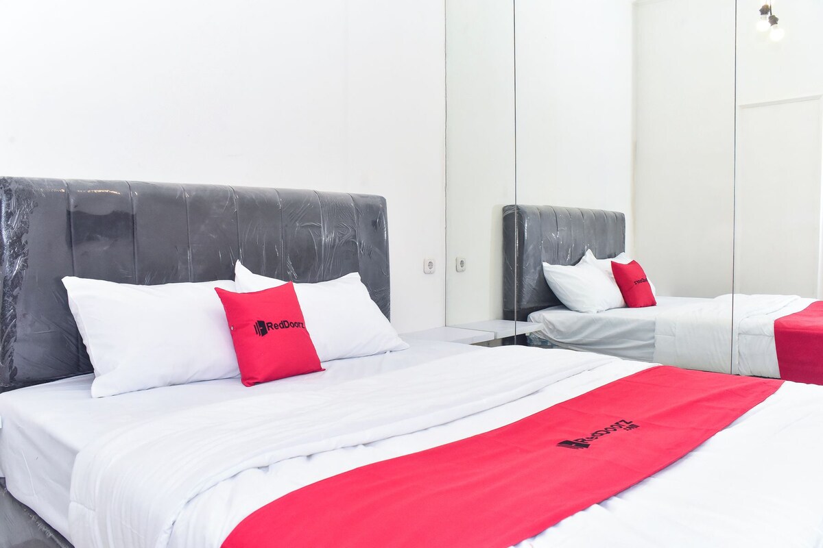 A hotel room with two beds, each with white bedding and red accents, and a large mirror reflecting the room.