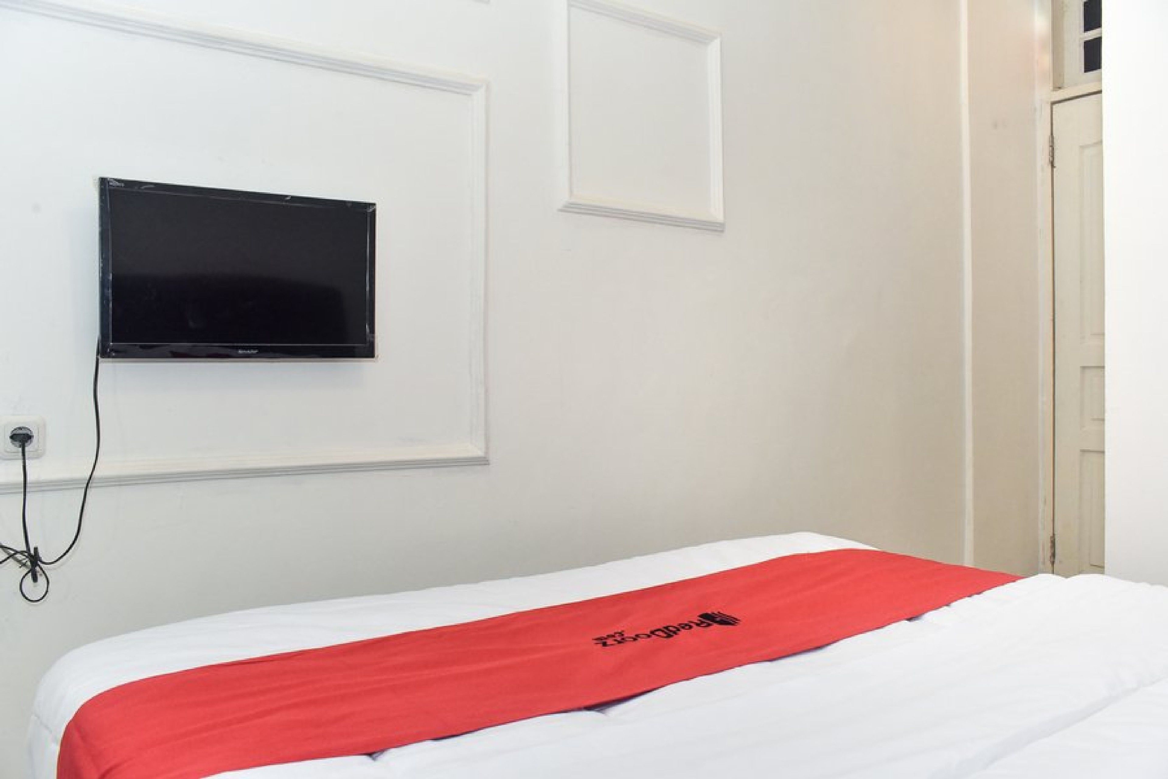 A hotel room with a bed, a television mounted on the wall, and a door.