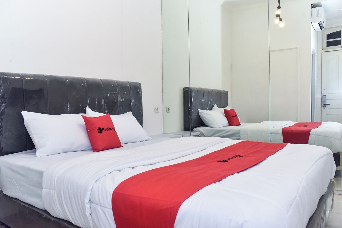 A hotel room with two beds, each with white bedding and red accents, a large mirror, and a ceiling-mounted light fixture.