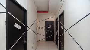 A narrow hallway with black doors and white walls, featuring a red accent on the ceiling. - RedDoorz Plus @ Kemayoran (Jakarta)