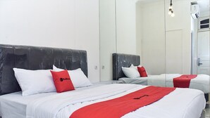 A hotel room with two beds, each with white bedding and red accents, a large mirror, and a modern design. - RedDoorz Plus @ Kemayoran (Jakarta)