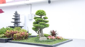 Ein angelegter Garten mit einer mehrstufigen Steinfontäne, einem Bonsai-Baum und verschiedenen bunten Pflanzen.