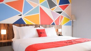 Ein Hotelzimmer mit Bett, weißer Bettwäsche, einer roten Decke und einem farbenfrohen geometrischen Wanddesign.