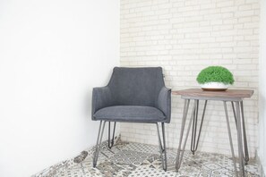 A grey upholstered chair with metal legs, a small round table with a potted plant, and patterned floor tiles. - RedDoorz Plus near UNIMED Medan (Medan)