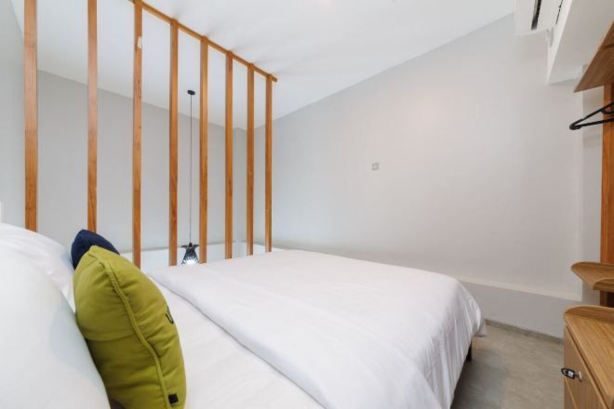 Un dormitorio con cama, cabecera de madera, cómoda de madera y lámpara colgante.