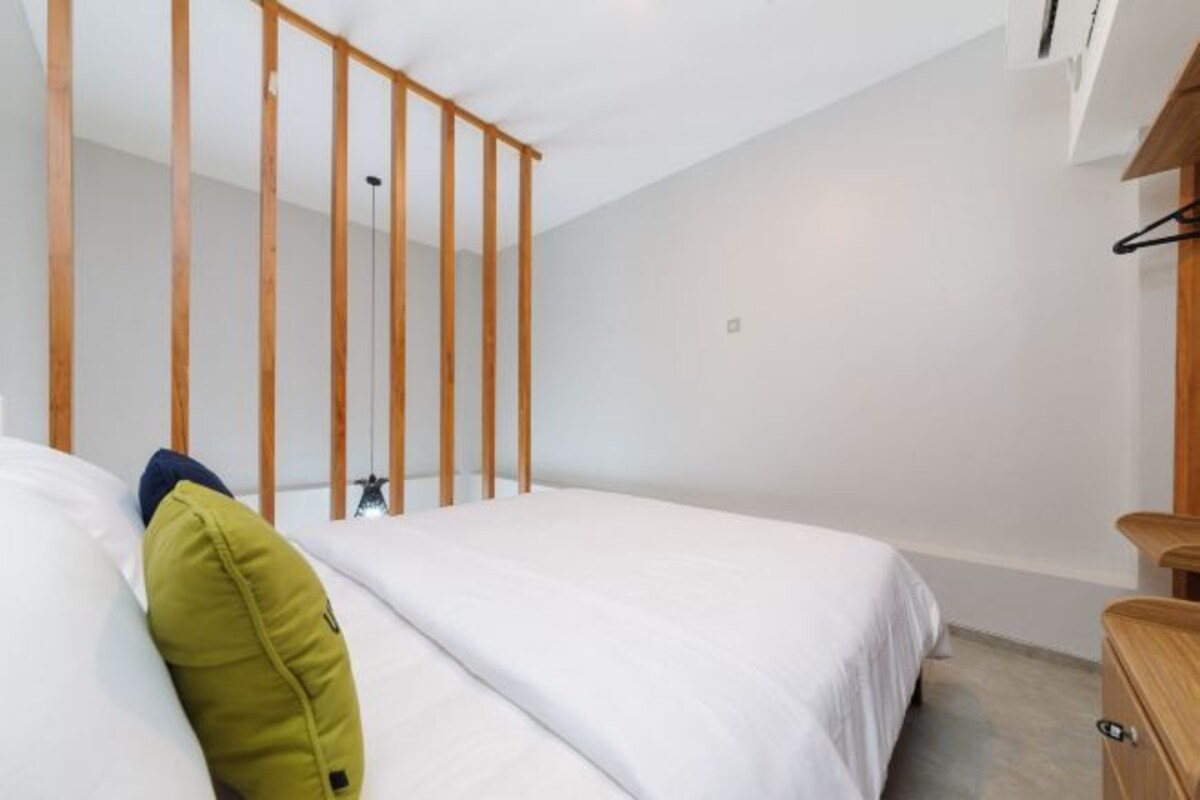 A bedroom with a bed, a wooden headboard, a bedside table, and a hanging light fixture.