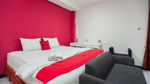 Une chambre d’hôtel avec un lit, une table de chevet, une chaise et un mur d’accent de couleur rouge.