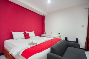 A hotel room with a bed, a nightstand, a chair, and a red accent wall.