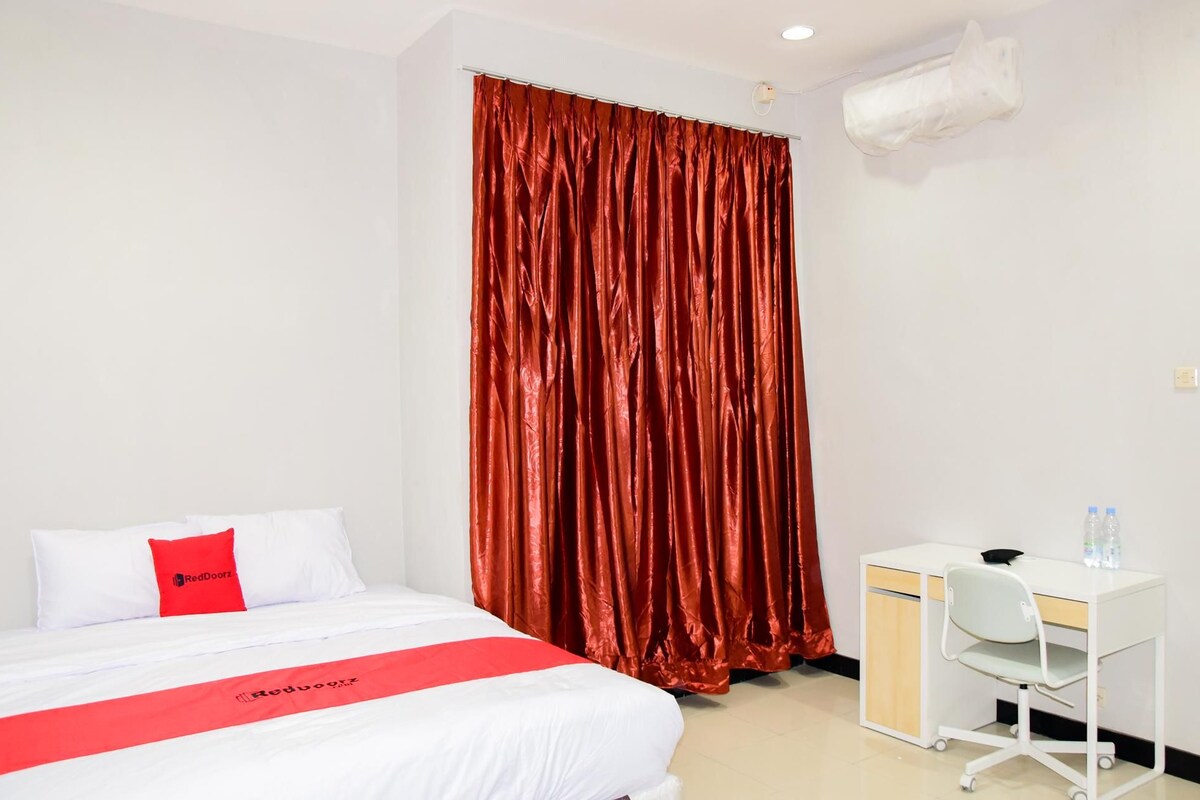 Une chambre d’hôtel avec un lit, un bureau et un rideau rouge.