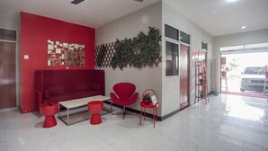 Un hall d’entrée moderne avec un canapé rouge, un fauteuil rouge, une petite table et un ventilateur de plafond.