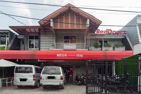 A building with a red awning labeled "RedDoorz" and "MEGA stay". There are two white vans parked in front, and several motorcycles inside. - RedDoorz Plus near Mall Kelapa Gading (Jakarta)
