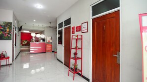 Un hall d'hôtel avec un comptoir d'accueil rouge, une porte en bois et une étagère métallique rouge ornée de plantes.