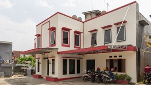 Un bâtiment à deux étages, doté d’une façade rouge et blanche, de nombreuses fenêtres et d’un espace d’entrée abrité où sont garées des motos.