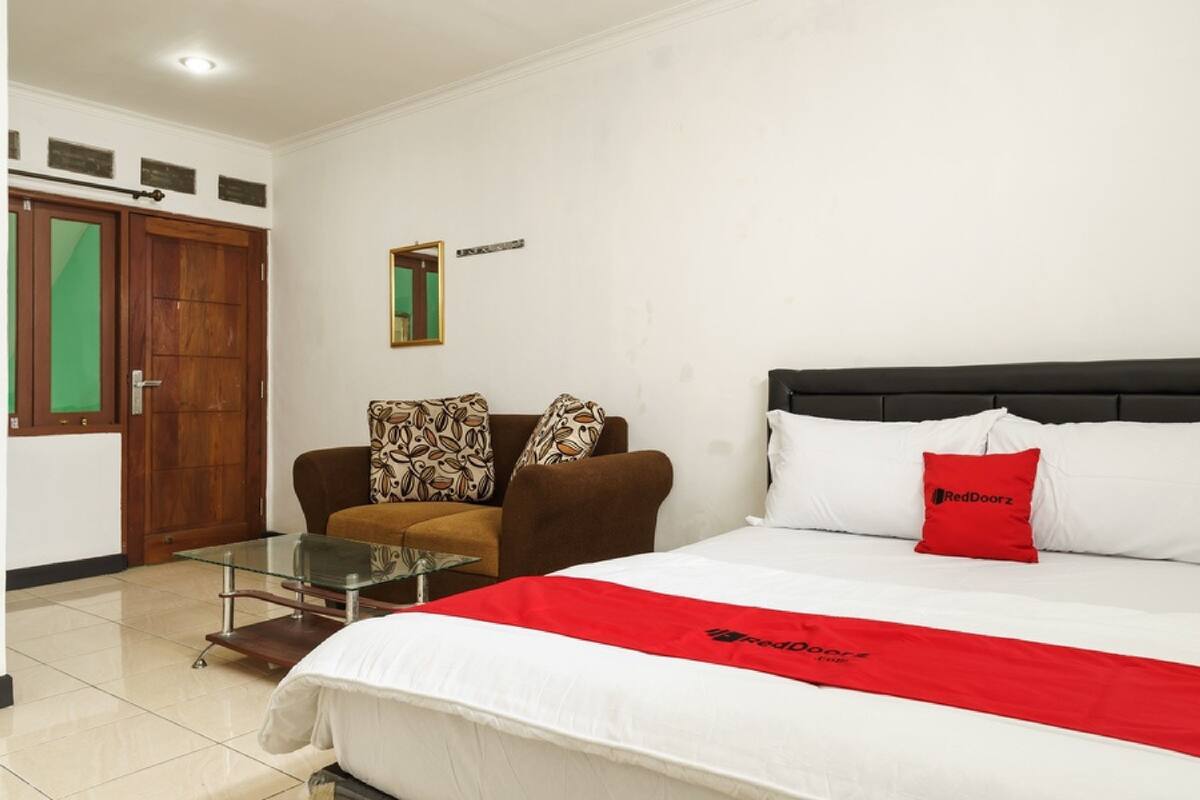 A hotel room with a bed, a sofa, a glass coffee table, and a door with a green glass panel.