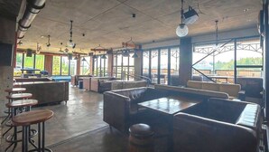 Un espacio interior amplio con techos altos, ventanas grandes y diversos arreglos de asientos, incluyendo mesas y sofás.