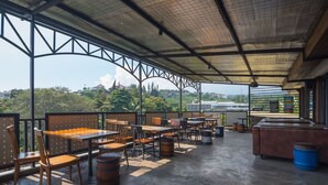 Un café al aire libre con mesas y sillas, un espacio de estar cubierto y vistas del paisaje circundante.