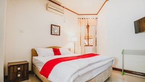 A neatly made bed with a white and red bedspread, a bedside lamp, and a small wooden nightstand. - RedDoorz Syariah near Gelora Delta Sidoarjo (Sidoarjo)